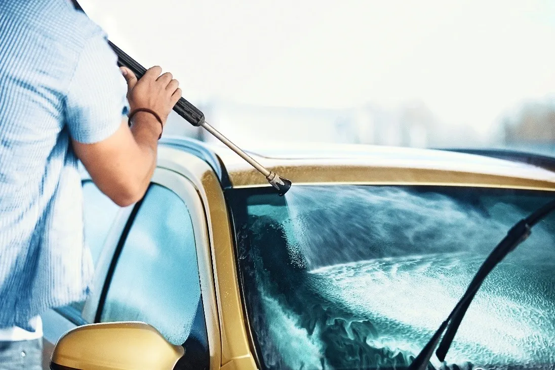 Customer washing a car with a high-pressure lance in a self-service bay
